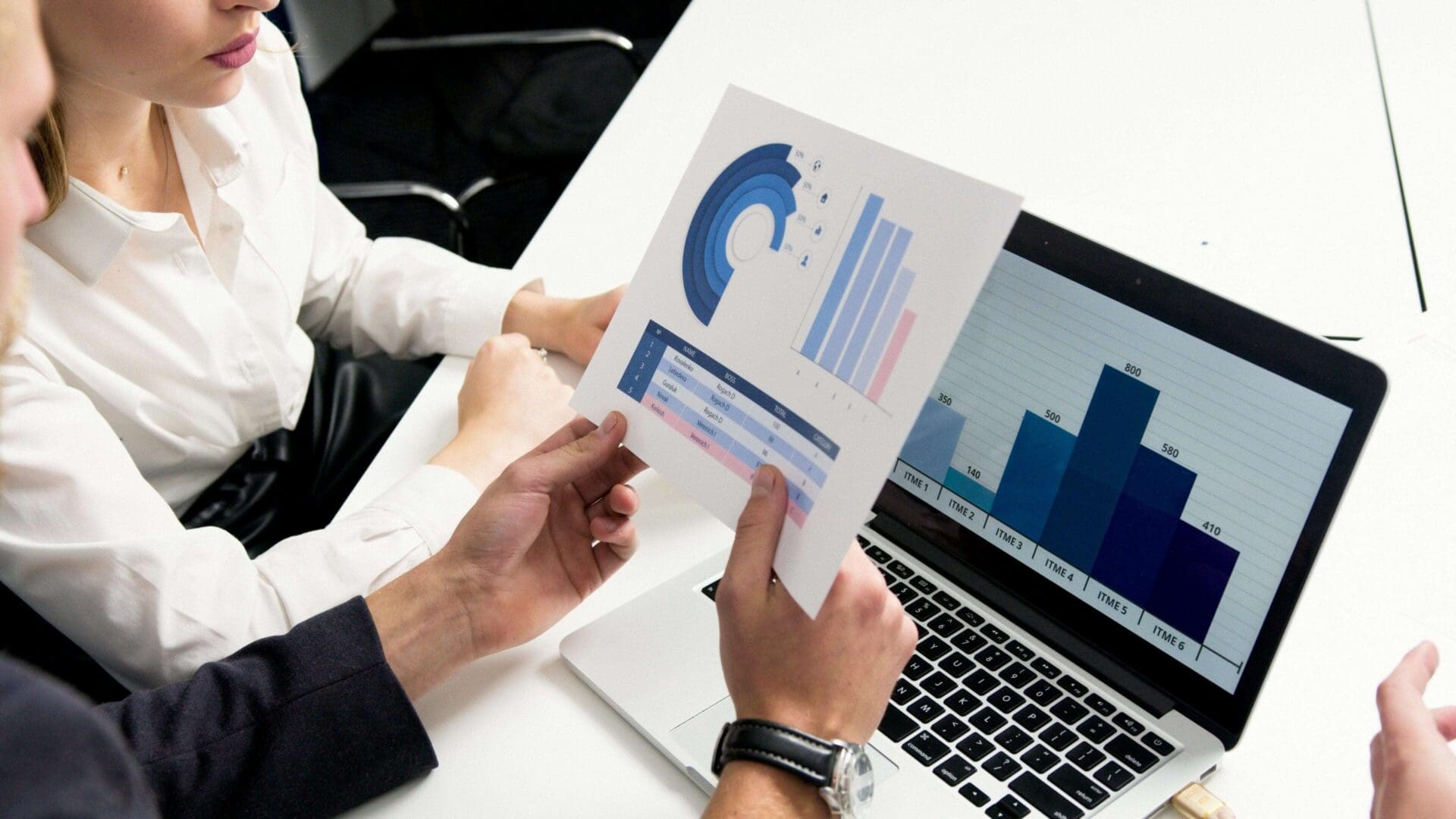 Two professionals analyzing financial charts and graphs on paper and laptop.