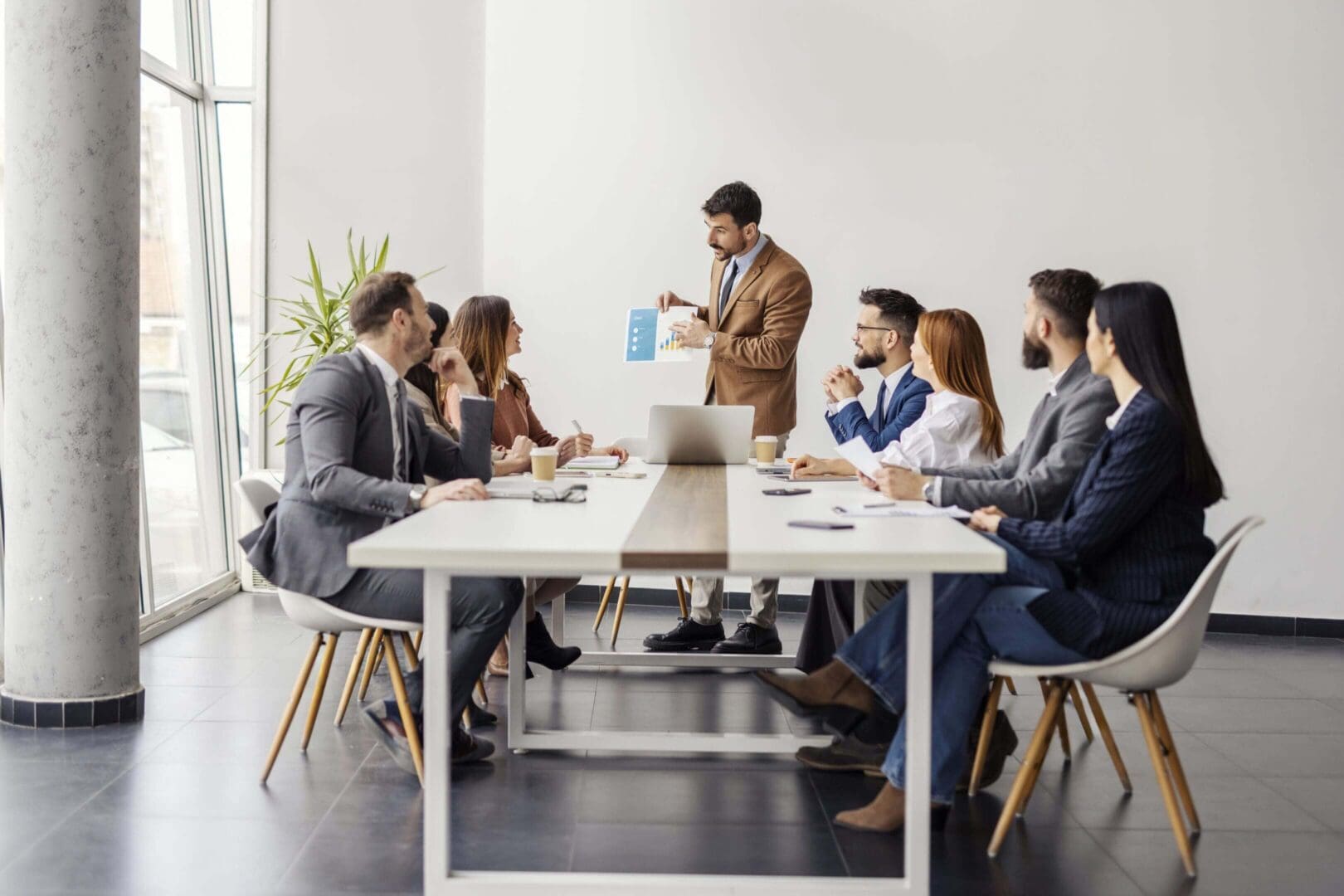 Business team engaged in a meeting with a presenter showing data on a tablet.